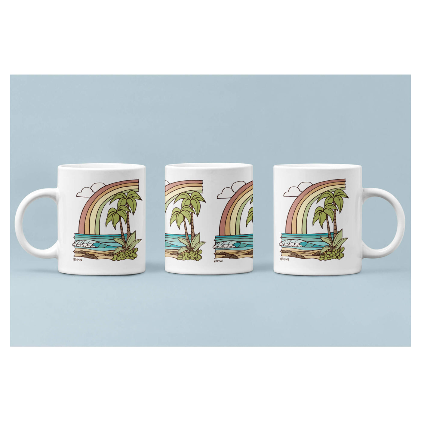 A white mug featuring a seascape with a rainbow by Hawaii surf artist Heather Brown