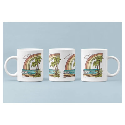 A white mug featuring a seascape with a rainbow by Hawaii surf artist Heather Brown