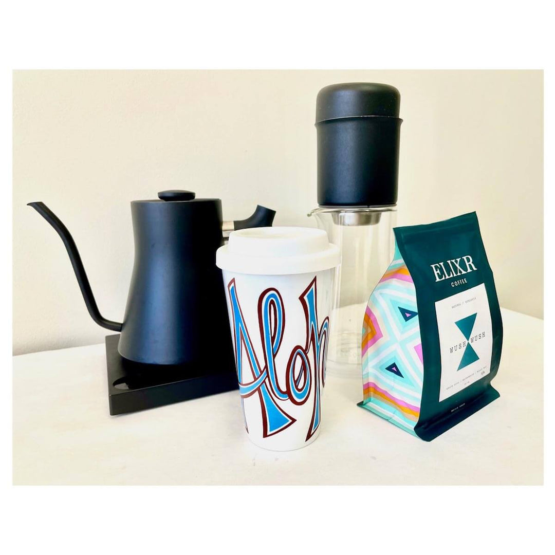 White ceramic coffee mug with Aloha word art by Heather Brown with coffee maker and kettle